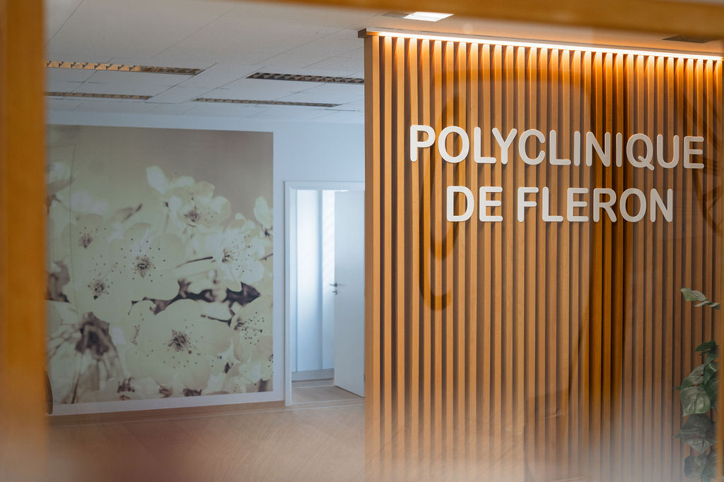 Enseigne intérieure « Polyclinique de Fléron » à l'entrée du bâtiment, avec fresque florale