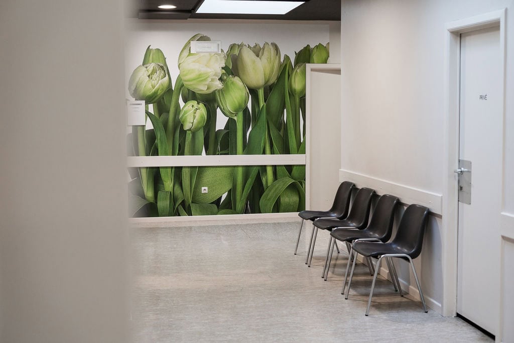 Couloir de consultations de la Polyclinique de Fléron, avec fresque florale et chaises d'attente